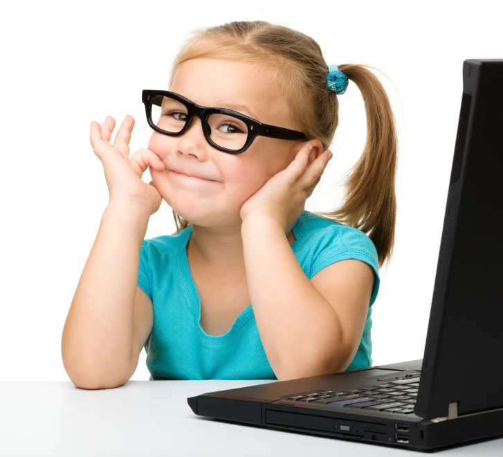 Cute little girl is sitting at table with her black laptop and wearing glasses, isolated over white
